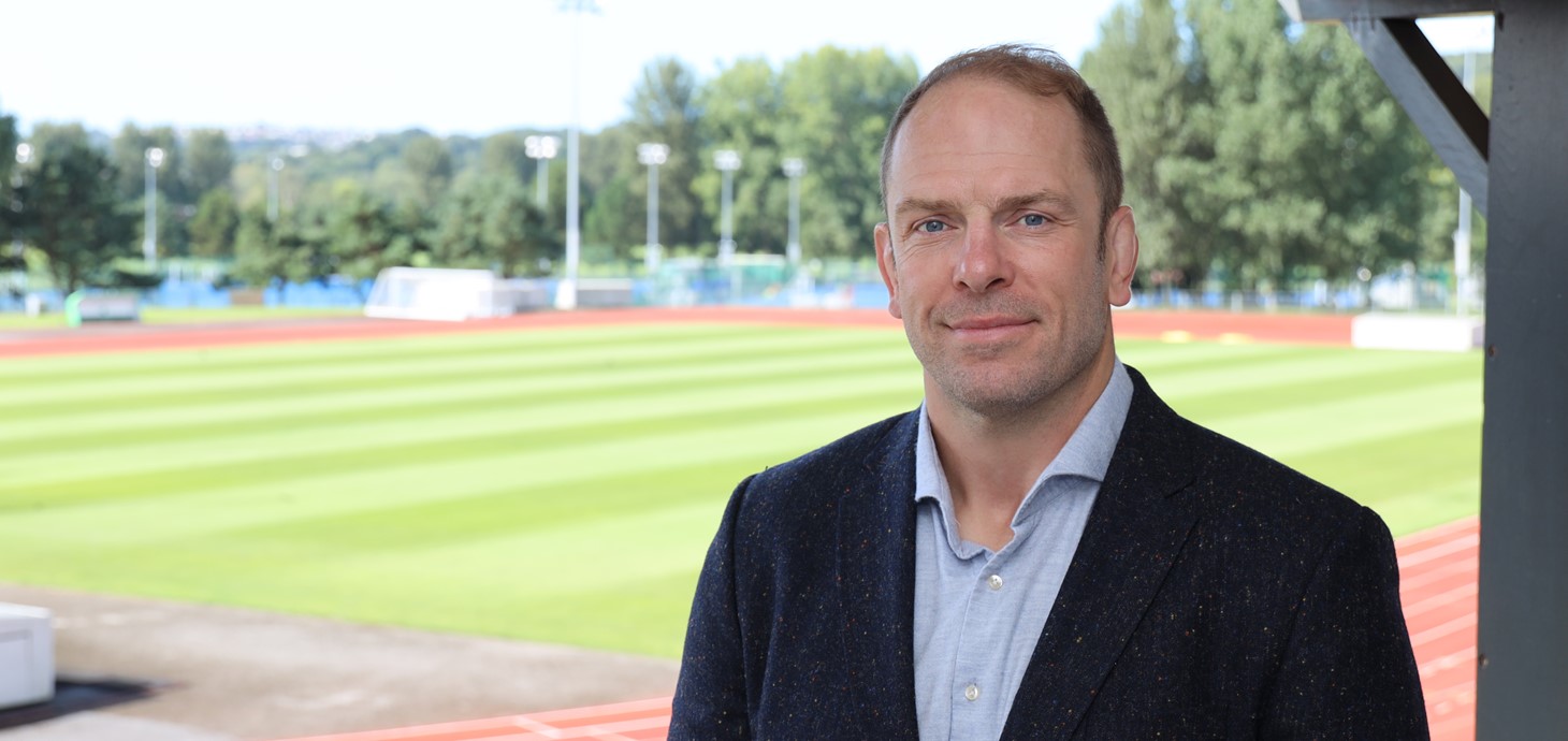 A headshot of Alun Wyn Jones wearing a suit. In the background is Swansea Bay Sports Park.