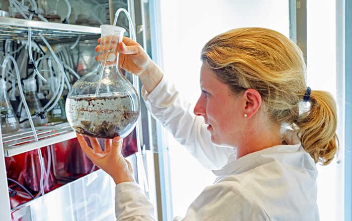 . A woman in a lab coat is holding a beaker