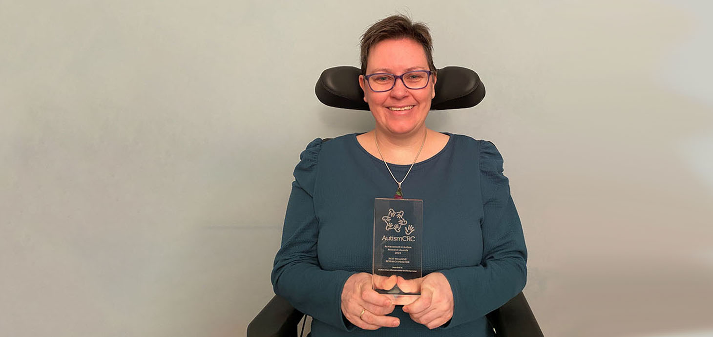 Alt-text Dr Aimee Grant is smiling as she holds her glass Autism CRC award. She is seated in her wheelchair. 