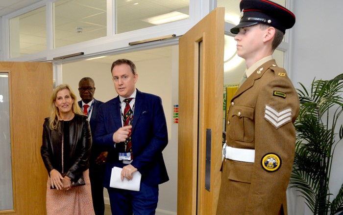 Woman and two men enter a room through a door held open by a military cadet