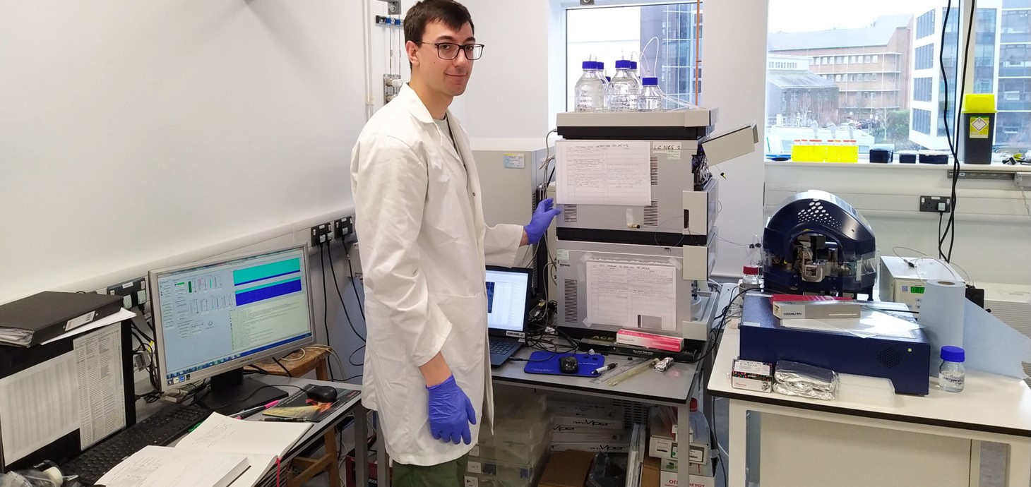 First-year SWBio student Tom wears a white lab coat and safety goggles as he works in the mass spectrometry lab.