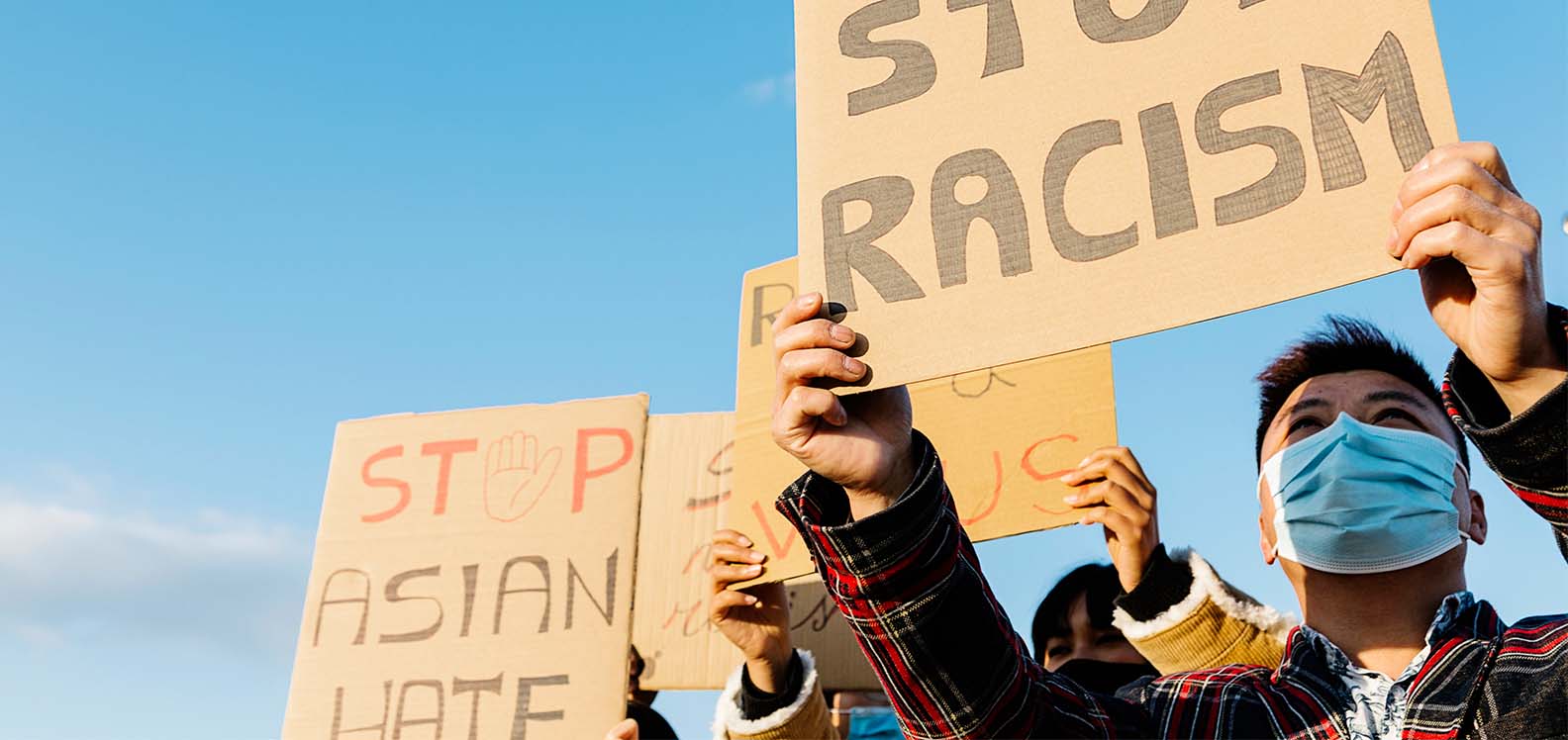 A male protestor from the ESEA community is wearing a face mask and carrying a sign saying ‘Stop racism’. Beside him is a placard with the message ‘Stop Asian hate.’
