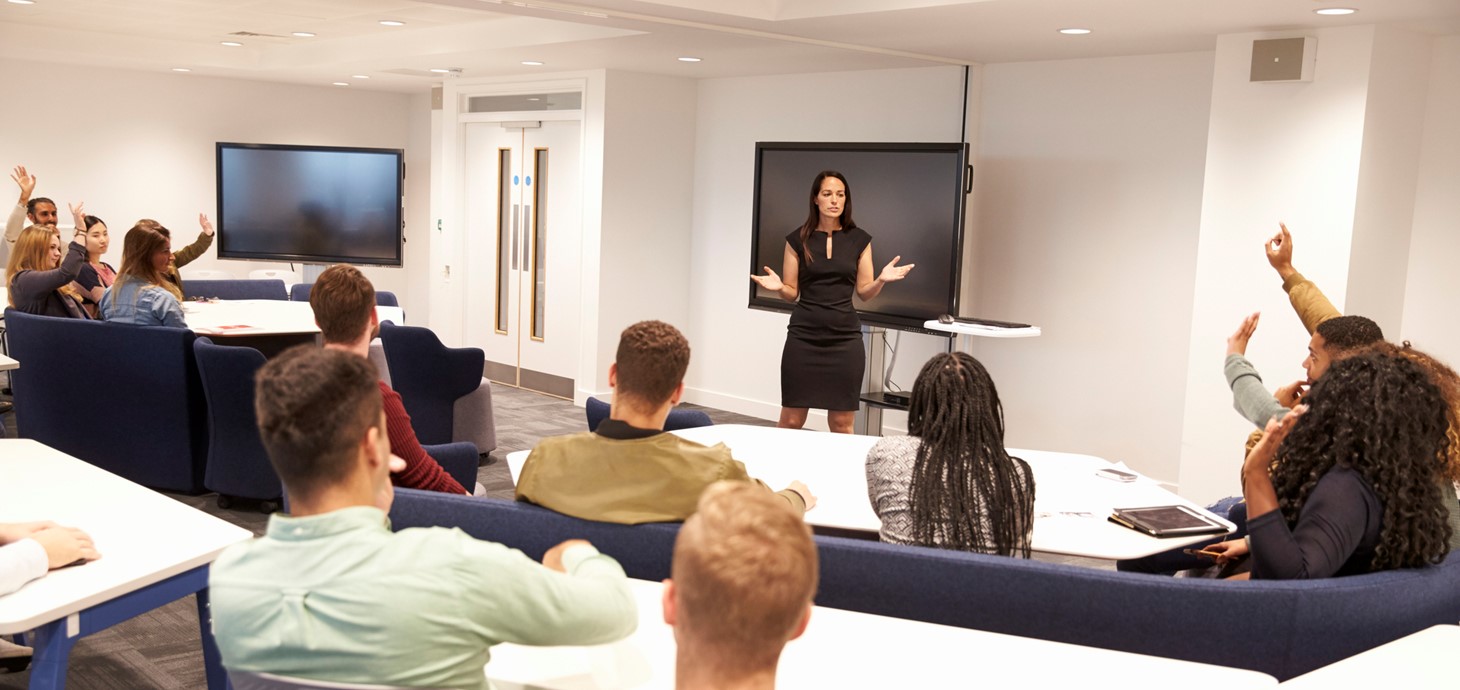 A female lecturer stands in front of a group of students in a lecture theatre