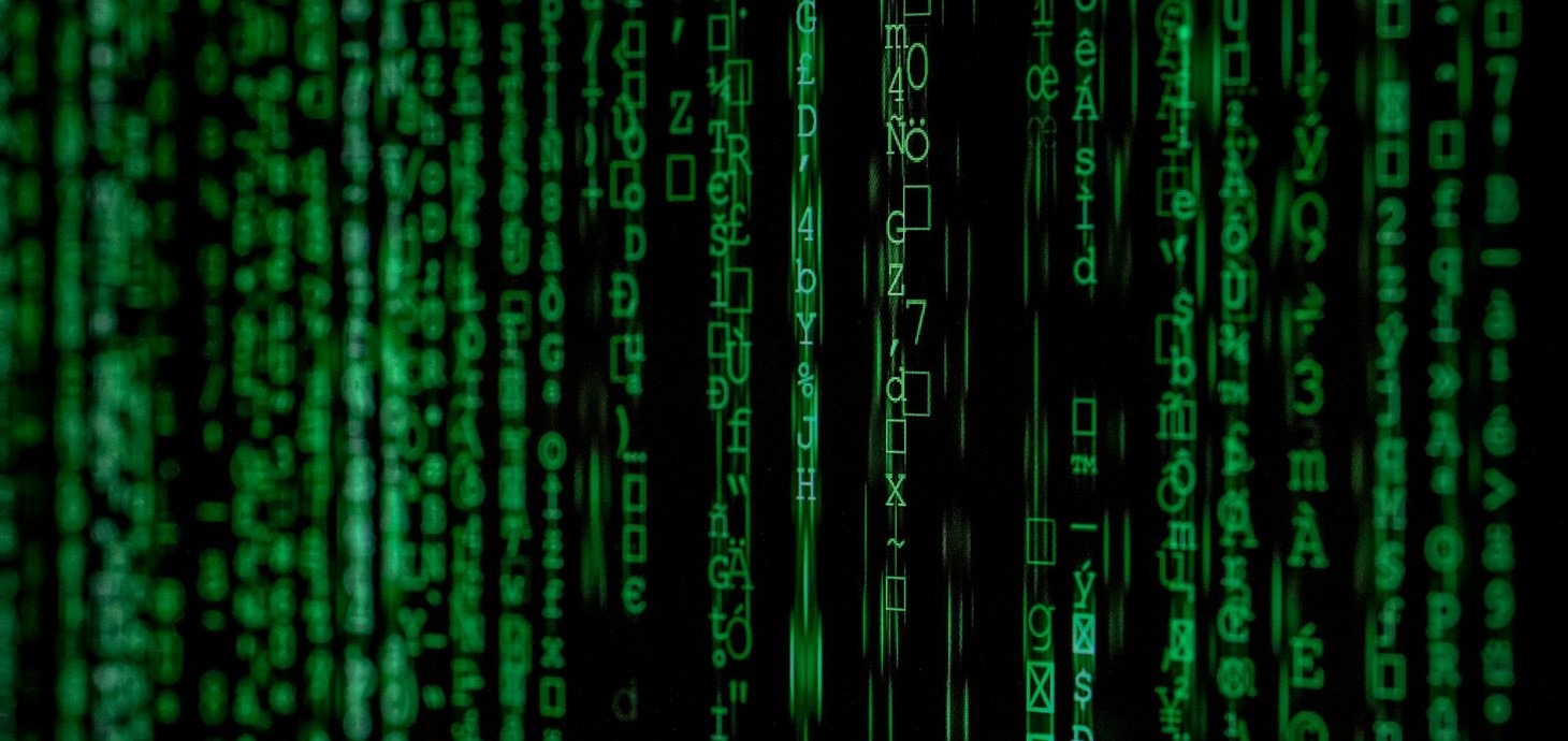 Green digital code characters cascade down a black screen, resembling the matrix-style computer code from the Matrix movie franchise.