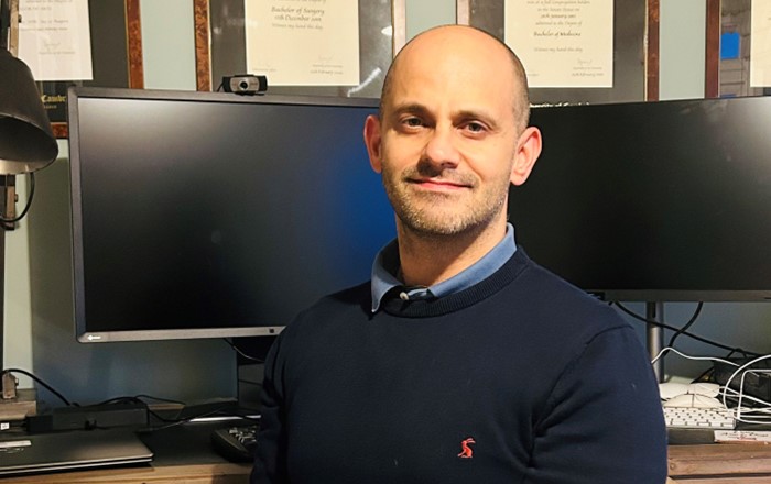 White man looking at camera in front of two computer screens.