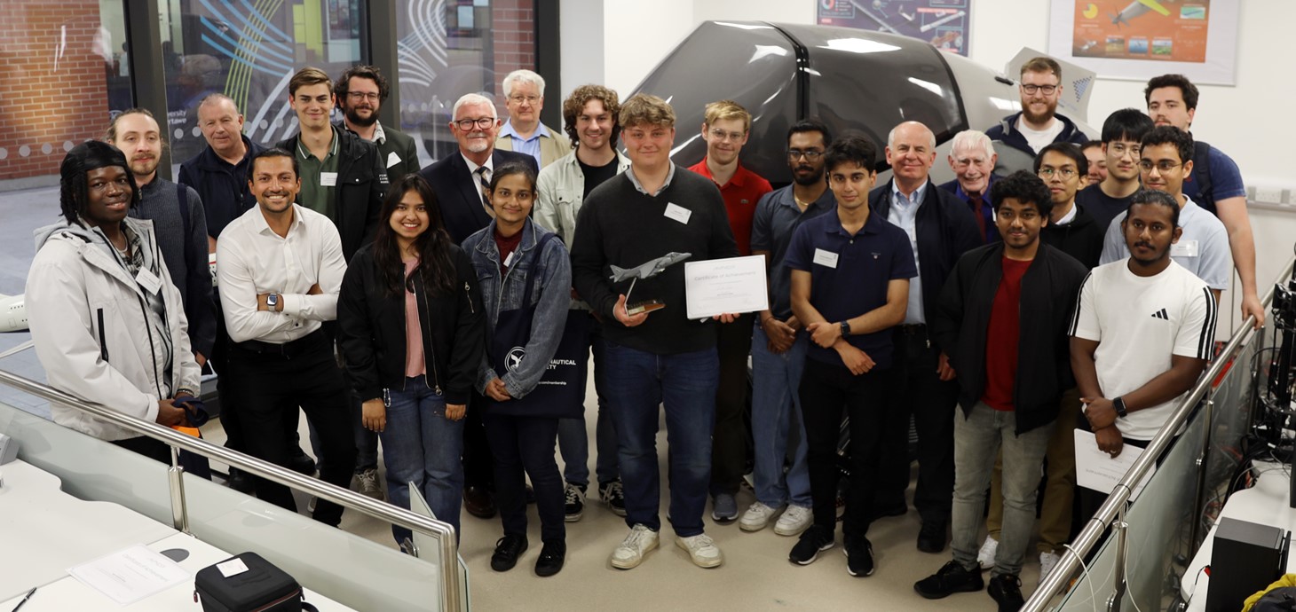 Group of 25 people of mixed ages standing in a room in front a flight simulator