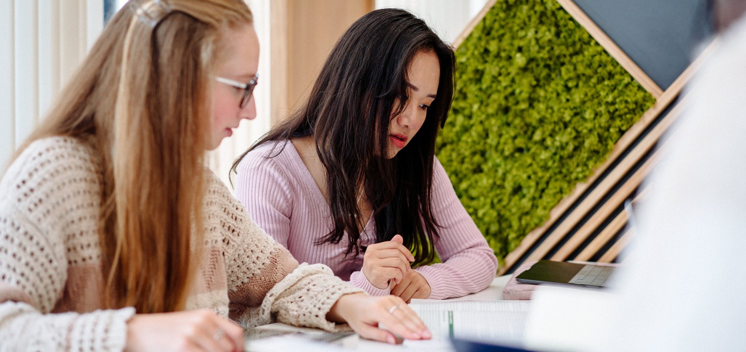 Two young women sitting side by side at a desk looking at a laptop screen