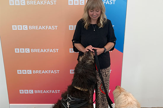 A picture of Dr Helen Lewis and her dogs Carlo and Obie at the BBC. Behind them is a banner with the BBC Breakfast logo.