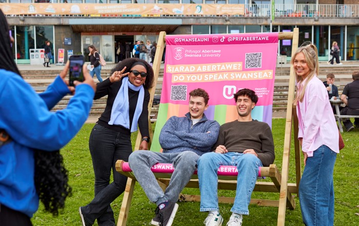 A small group of happy-looking students sitting on a giant, colourful deckchair outside Fulton House
