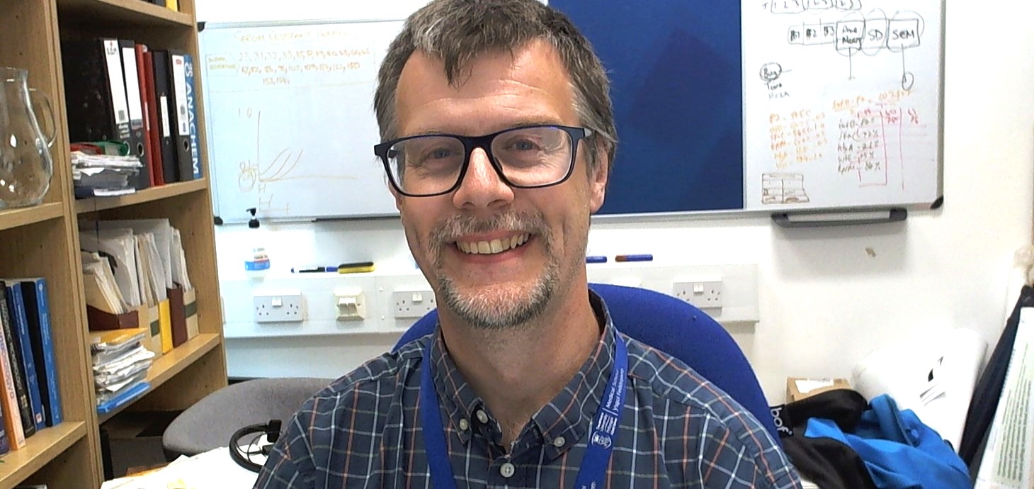 Man sitting in an office with whiteboard behind him 