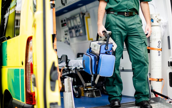 Paramedic holding medical equipment stepping out of an ambulance.