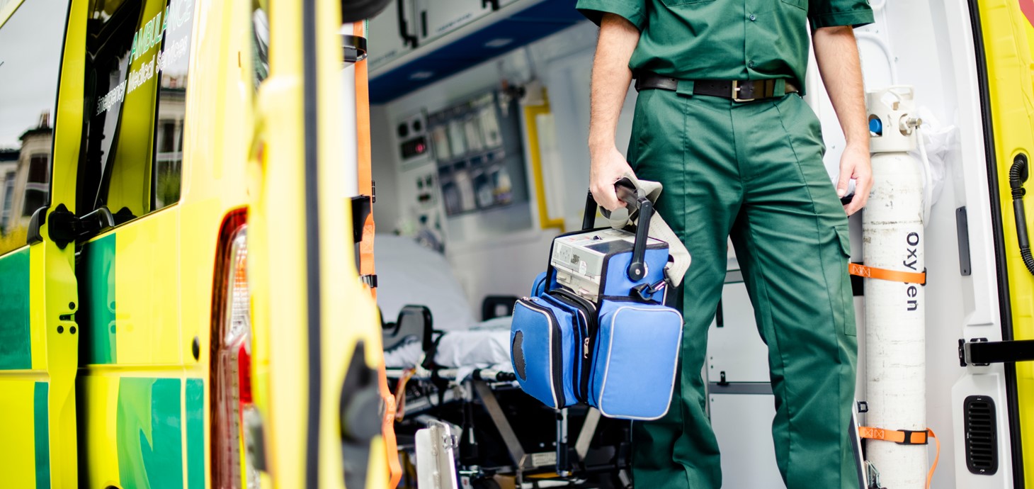 Paramedic holding medical equipment stepping out of an ambulance.