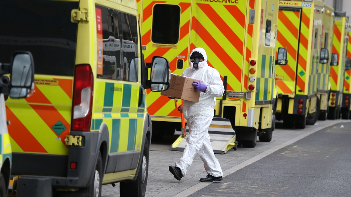 An emergency services staff member wearing PPE runs through parked ambulances outside Royal London Hospital. (Credit: I T S | Shutterstock).