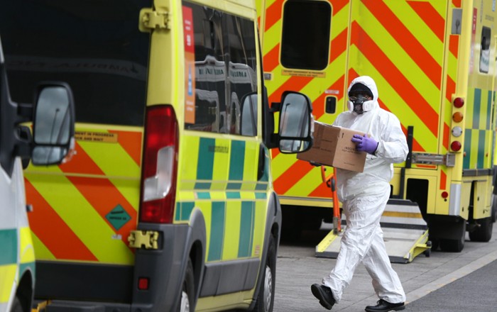 An emergency services staff member wearing PPE runs through parked ambulances outside Royal London Hospital. (Credit: I T S | Shutterstock).