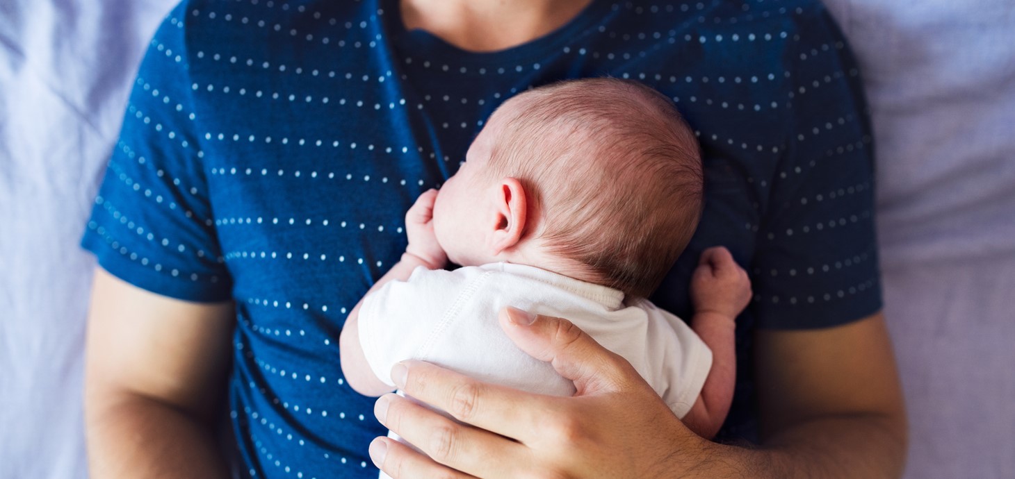 An unidentifiable man with a sleeping baby on his chest