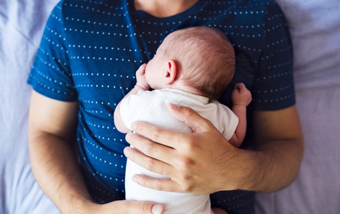 An unidentifiable man with a sleeping baby on his chest