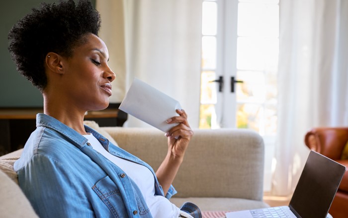 A menopausal mature woman at home looking at a laptop while having a hot flush and fanning herself.
