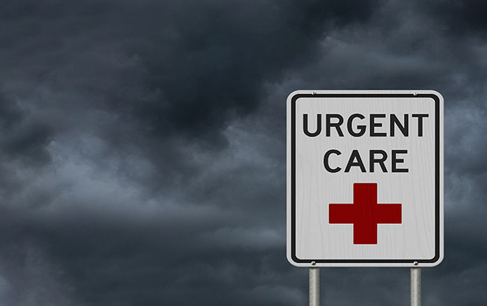 A rectangular white sign which has a red cross and URGENT CARE on it.