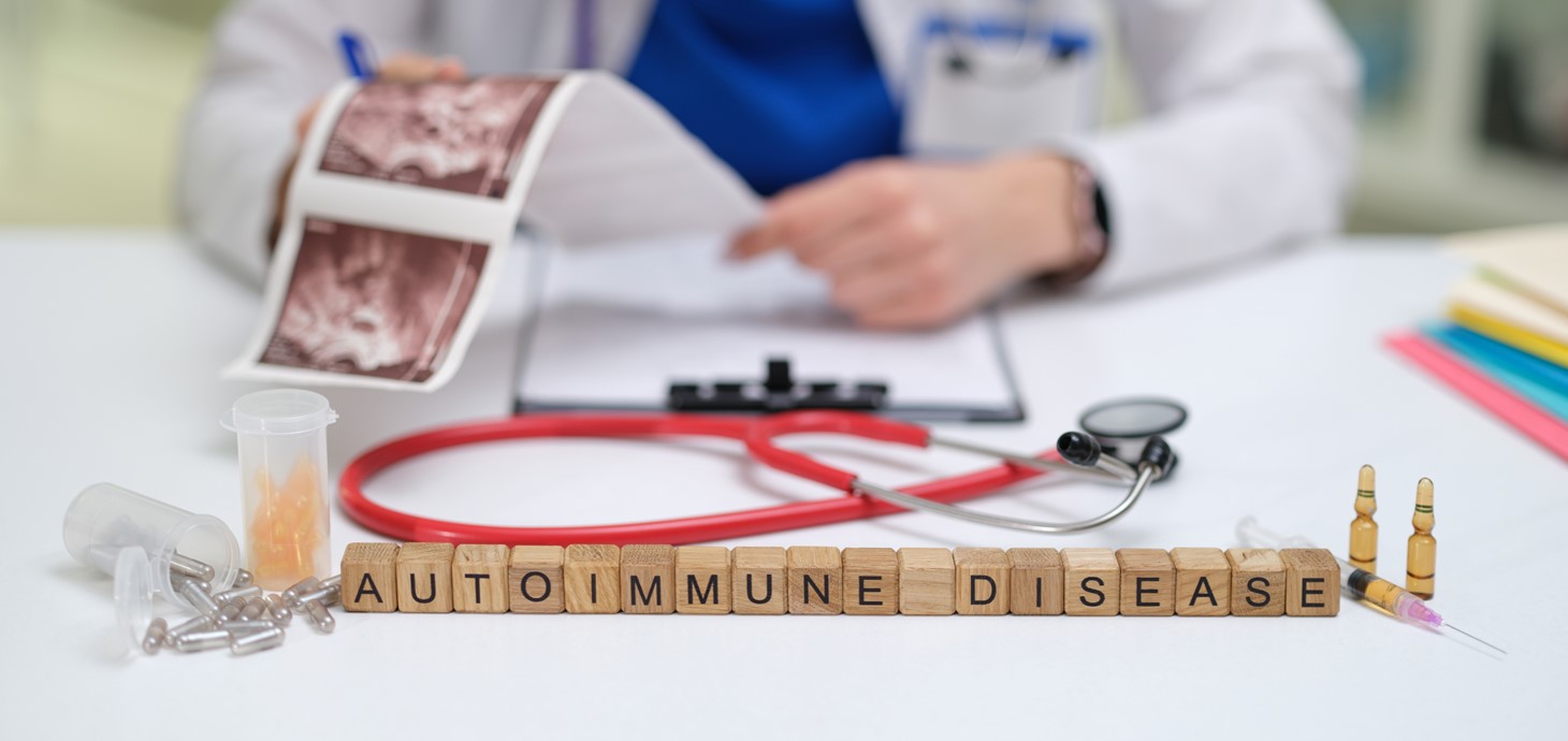 A wooden sign with the words 'autoimmune disease' is on a desk in front of a doctor who is reviewing information on autoimmune diseases.