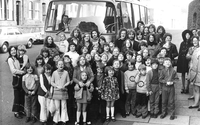Group of children and young people standing in front of a bus, black and white, taken in 1970s.