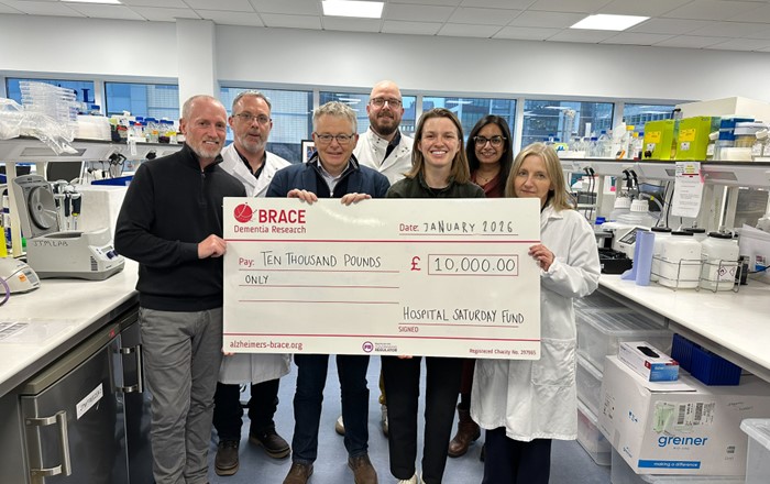 Group of seven people standing in a lab holding a large cheque