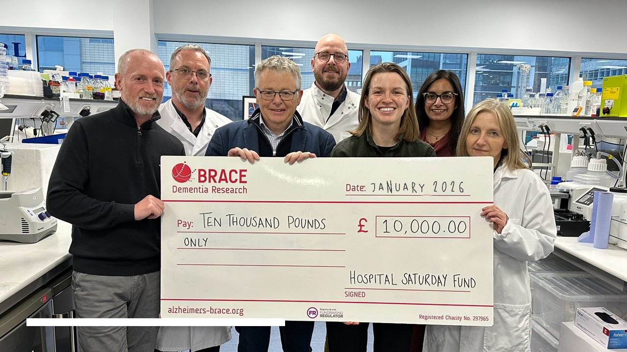 Group of seven people standing in a lab holding a large cheque