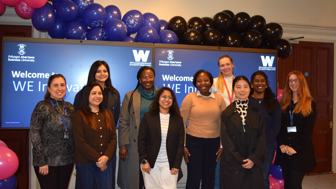 Group of 10 smiling women standing indoors front of banners and balloons