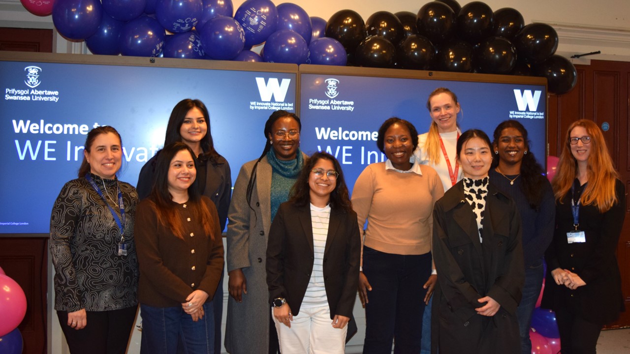 Group of 10 smiling women standing indoors front of banners and balloons
