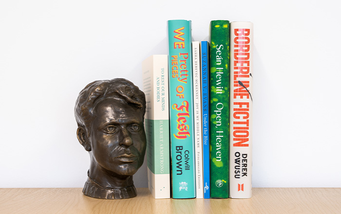 The six shortlisted titles lined up on a bookshelf next to a small bust of Dylan Thomas
