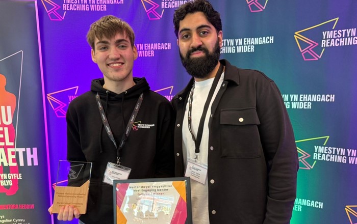 Two young men standing together in front of banner