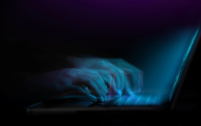 An abstract image of a person's hands typing on the keys of a laptop