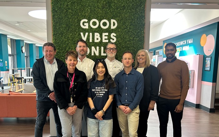 Eight people standing indoors in front of a large sign