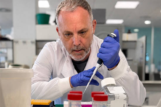 Man in white coat wearing gloves and using lab equipment.