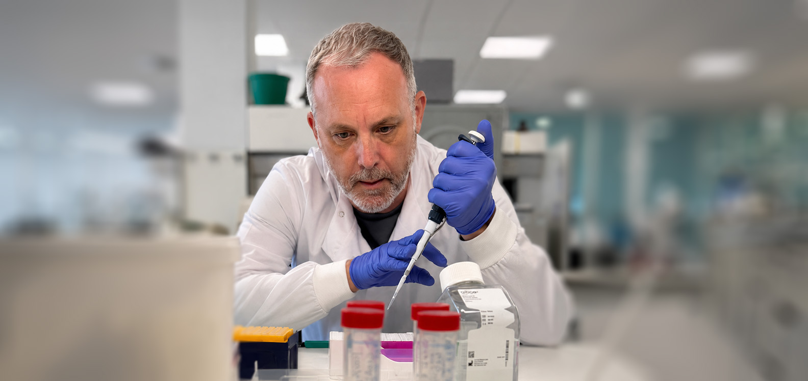 Man in white coat wearing gloves and using lab equipment.