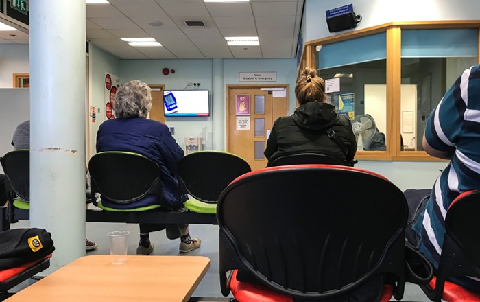 People sitting in a hospital waiting room with a reception desk in the corner.