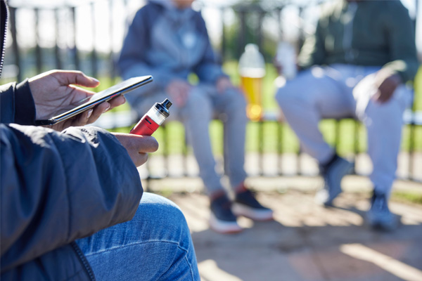 Close Up Of Teenagers With Mobile Phone Vaping