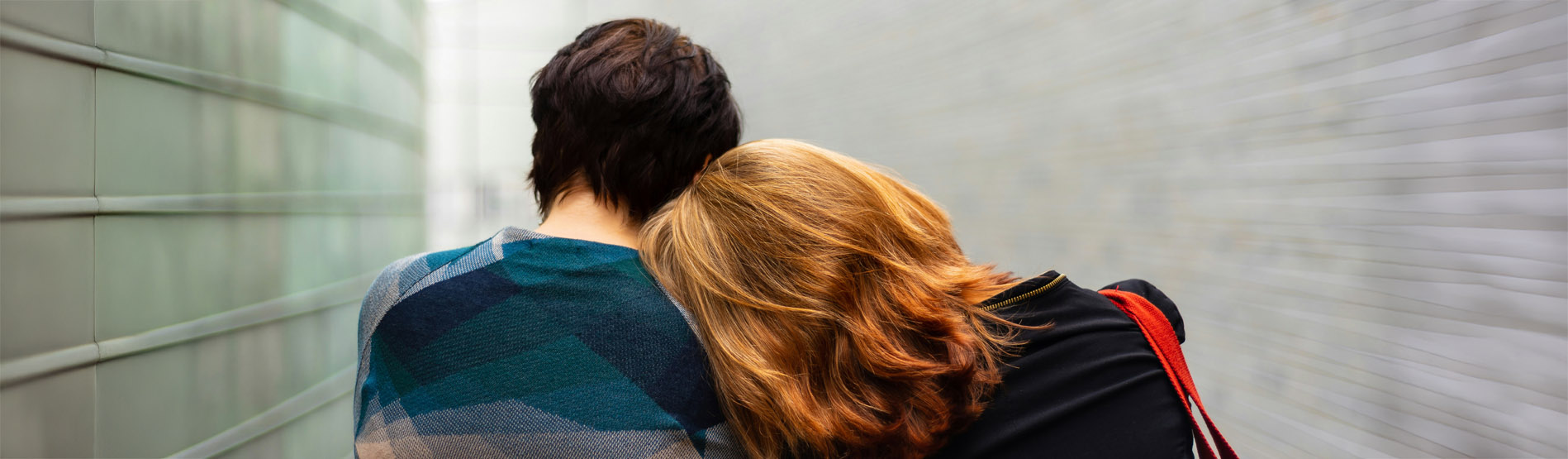 A photo from behind of a woman resting her head on a man's shoulder