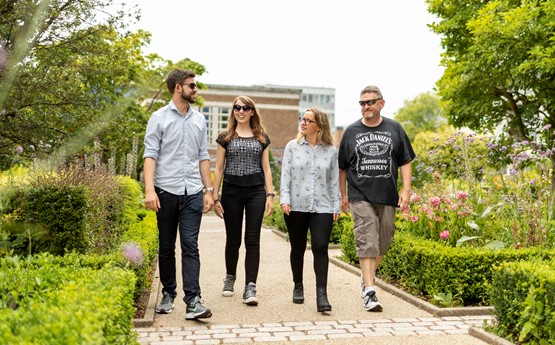 four people walking in line down a path surrounded by bushes