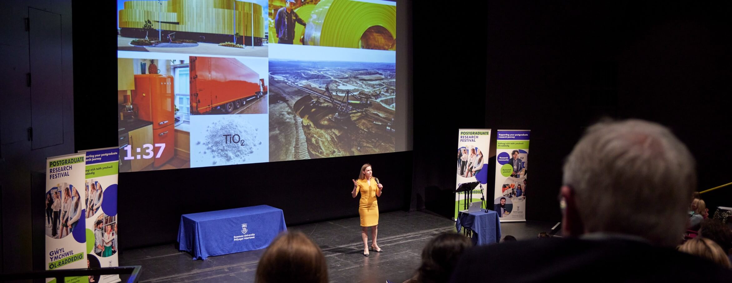 A student delivering a presentation on a large stage, images behind on a large screen.