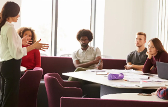 A teacher talking to her students who are sat around a table