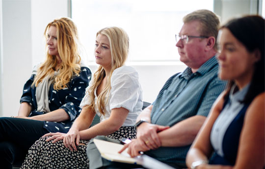 Three woman and a man sitting in a row listening to someone off camera