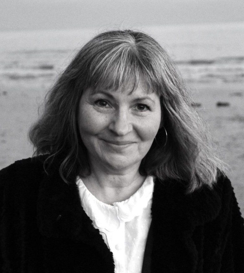 A headshot of a White woman in her mid-fifties taken on a windswept beach. 