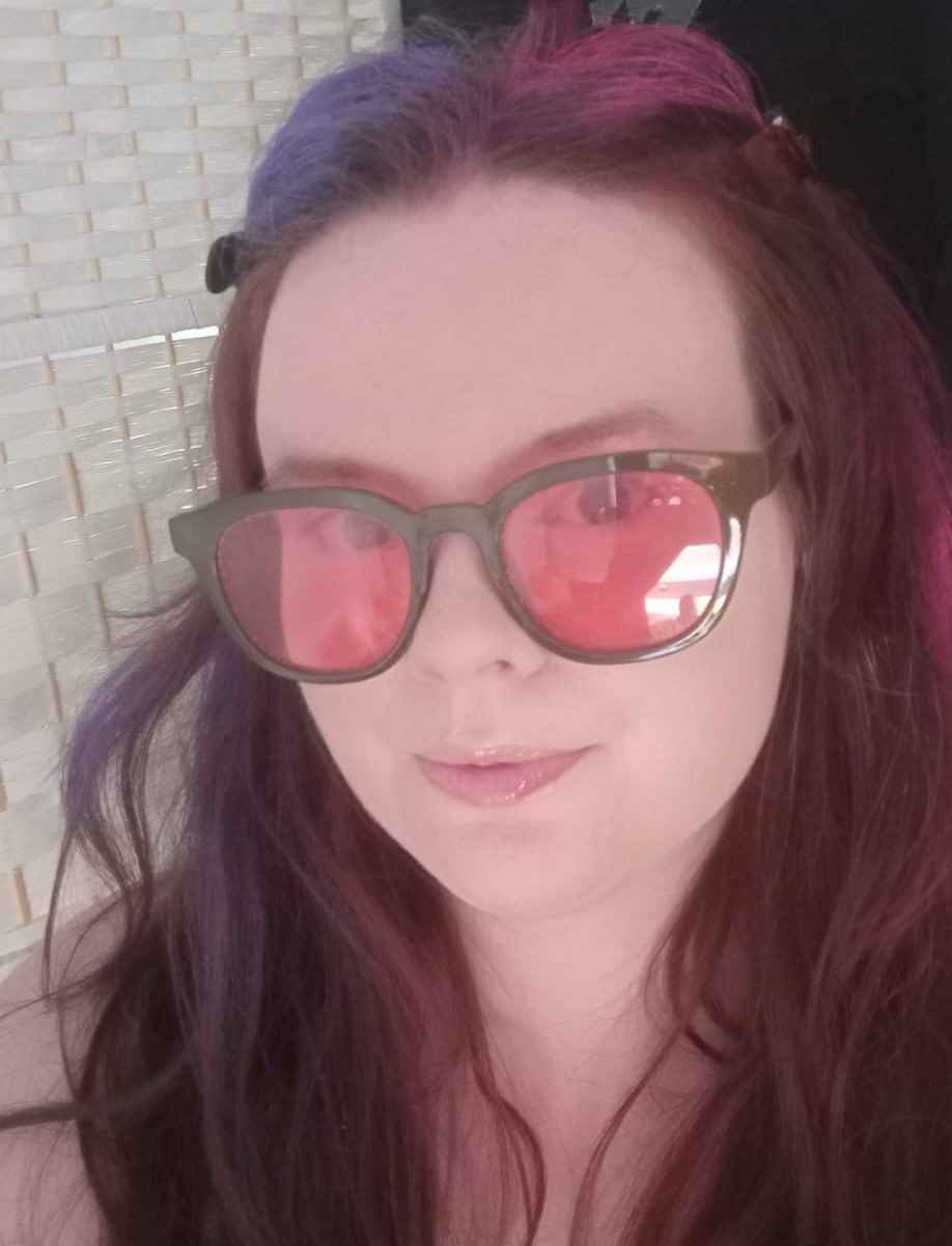 A white person with red hair wearing pink tinted glasses 