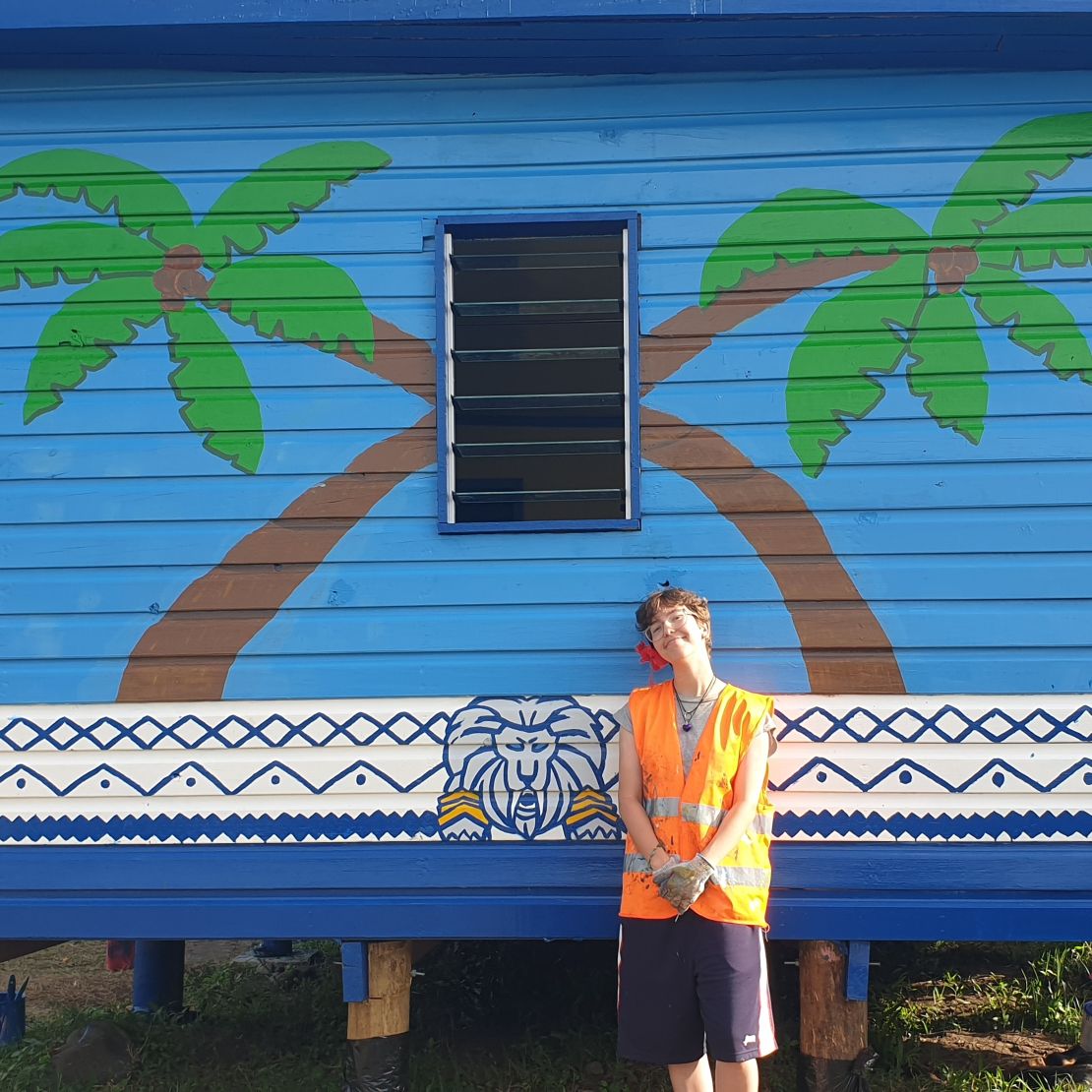 Student in Fiji standing in front of a palm tree mural.