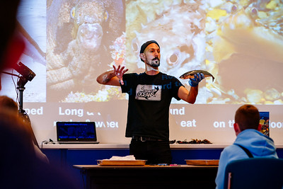 A speaker on a stage with a fish in his hand