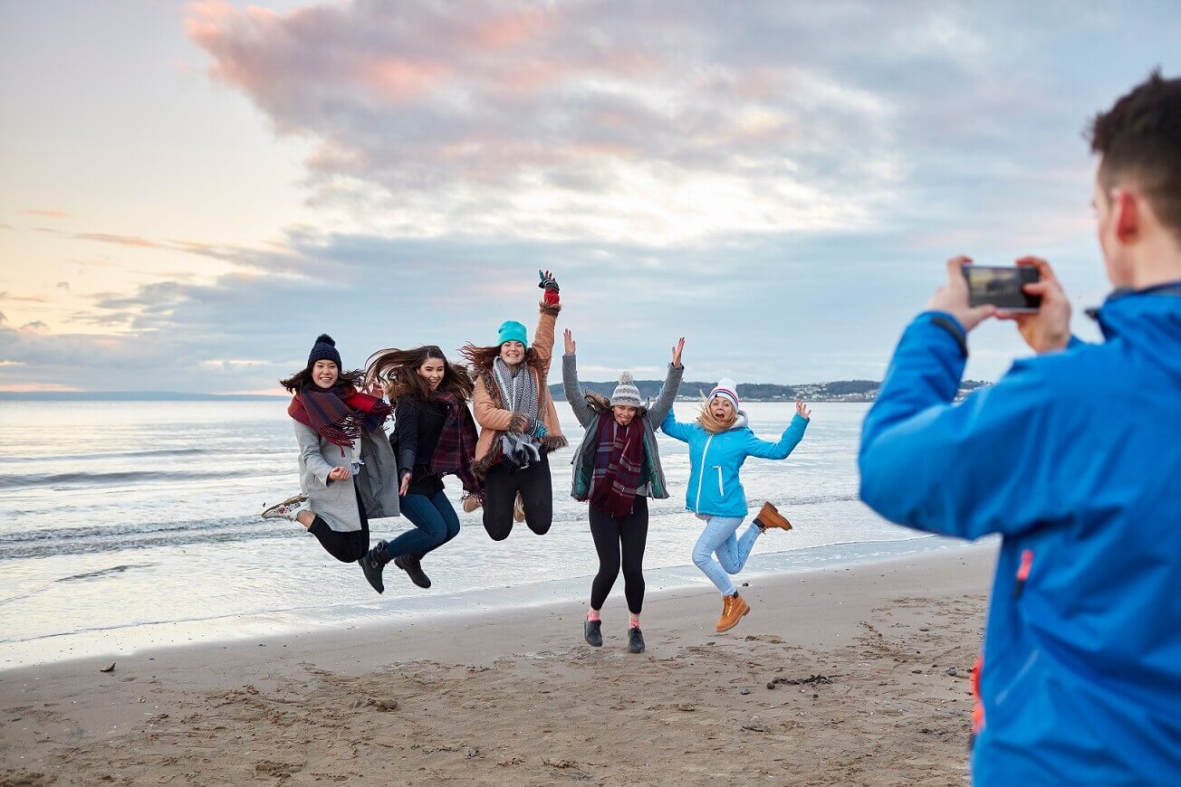 Students jumping for joy on the beach in winter