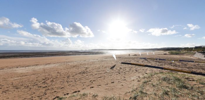 Wide sandy beach with calm sea, dunes, and bright sky in sunlight