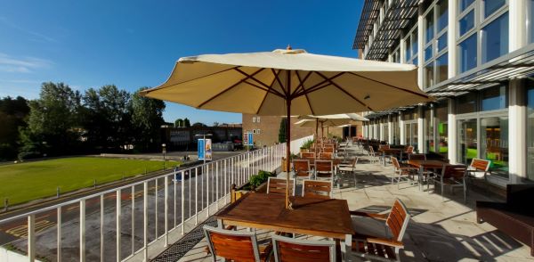 Outdoor terrace with wooden tables and parasols beside a modern building 