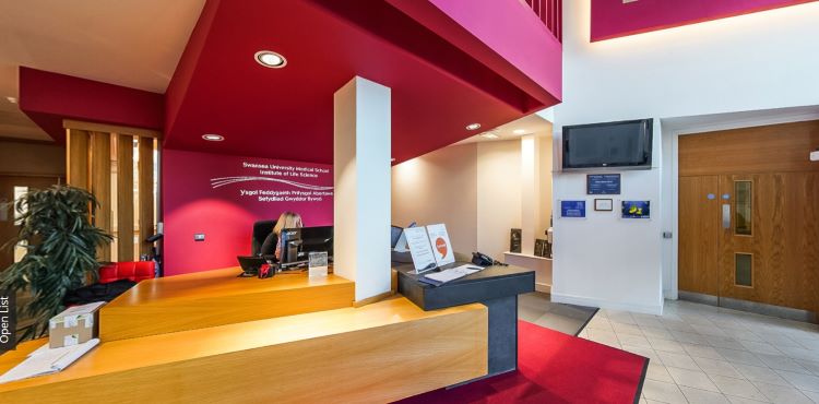 Reception area with desk, red walls, signage, seating, and wall-mounted screen