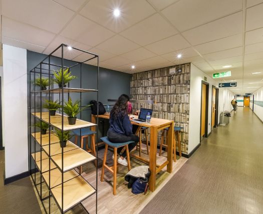 Workspace with shelving, tall table, and a laptop user